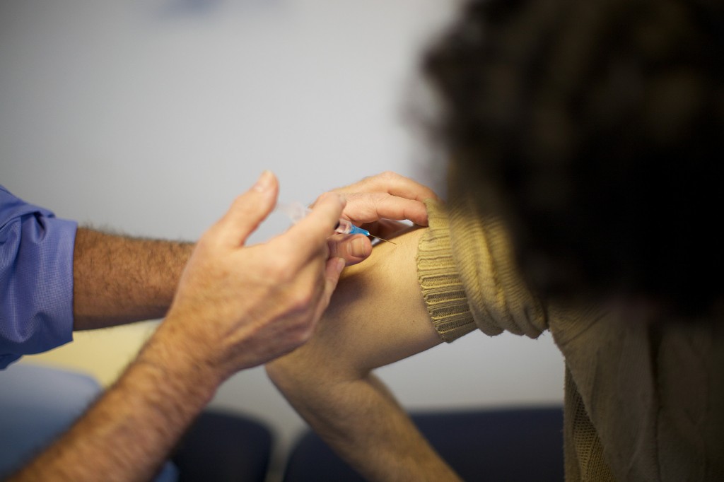 A person's arm with sleeve rolled up. A medical professional with sleeves rolled up is giving the person a vaccine.