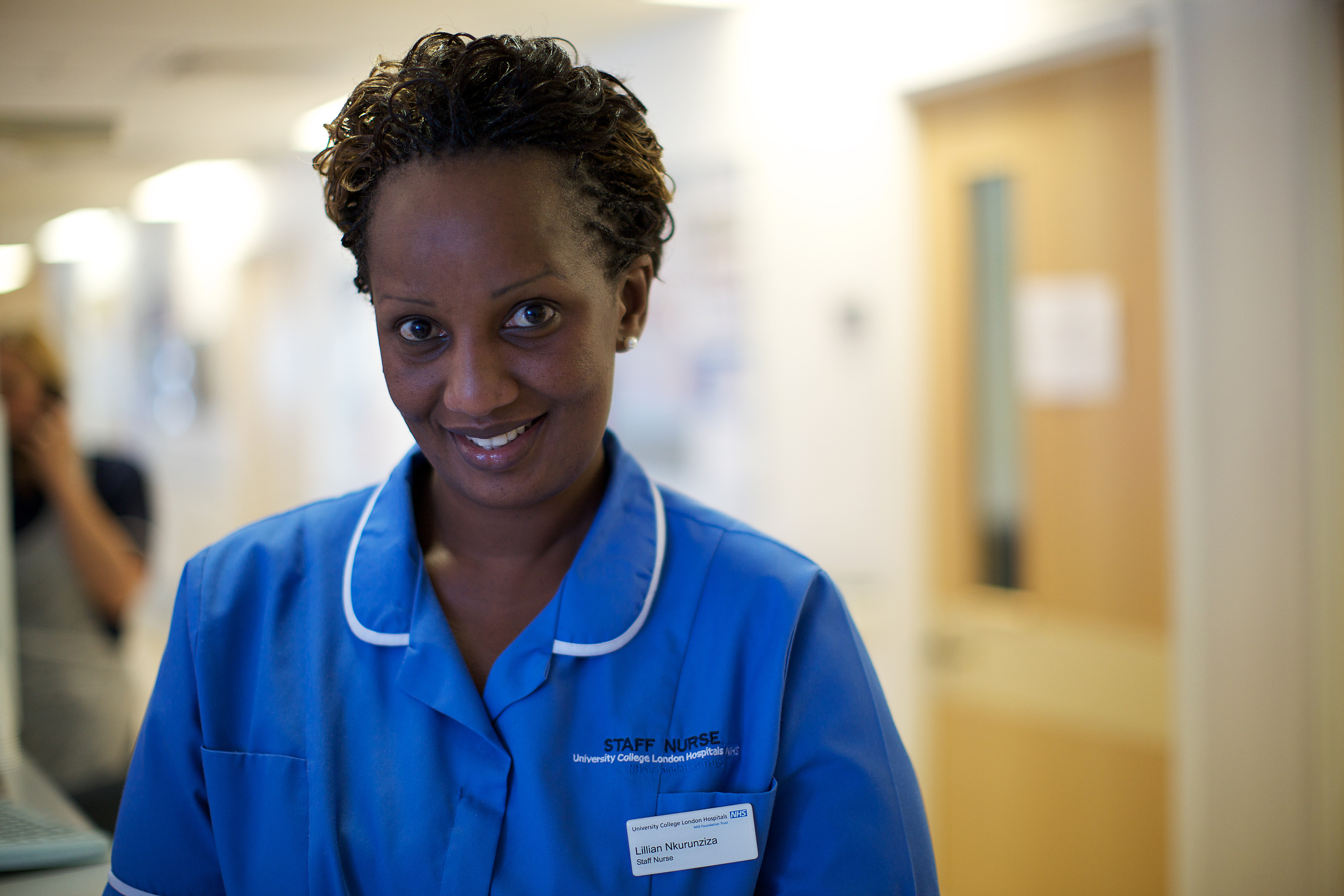 Unique ID: NHS_UCLH_DAY 1 STAFF_0083 Caption: A woman in a hospital corridor. Wearing a bright blue uniform. A nurse with a badge. Restrictions: Copyright: ©