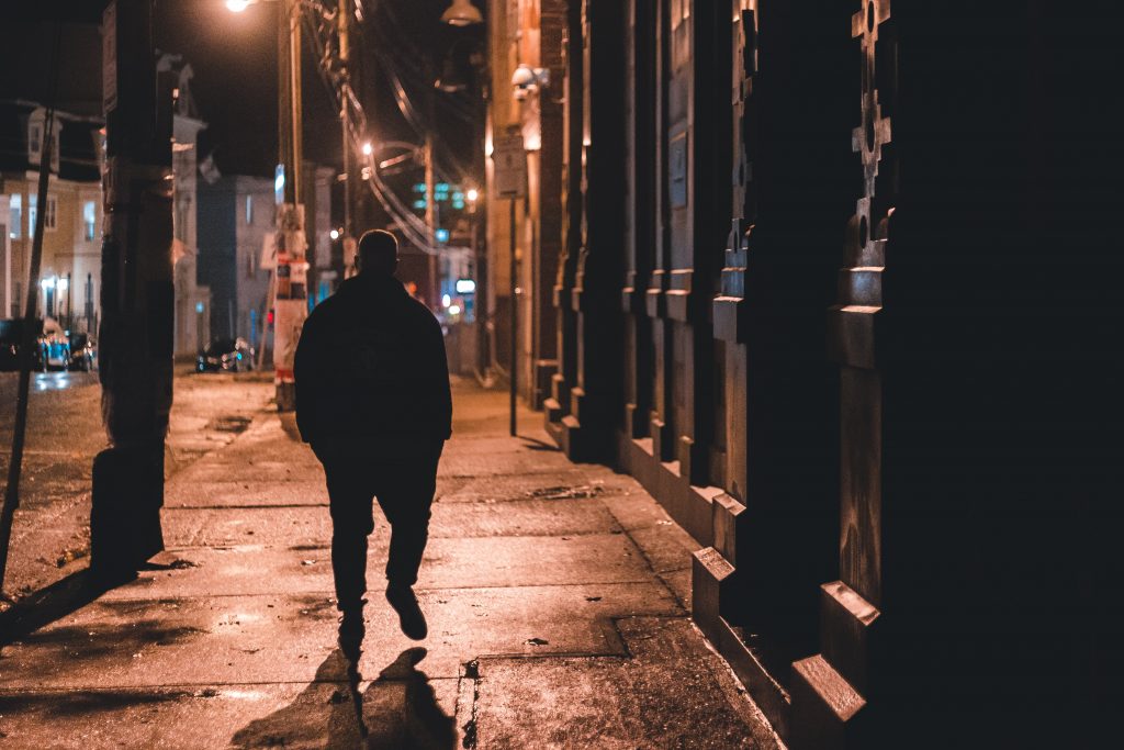 Person walks down a street at night, photographed from behind