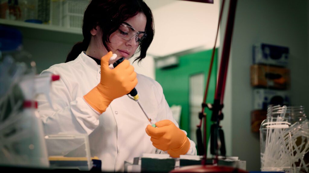 Woman in a white lab coat and orange gloves working in a laboratory