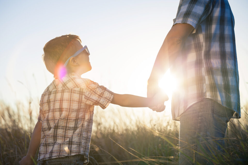 A man and child both in blue and white checked shirts, walking through a field during a sunset