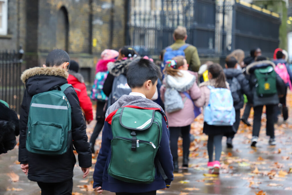 Un groupe d'écoliers en manteaux d'hiver et sacs à dos marchant dans une rue humide.