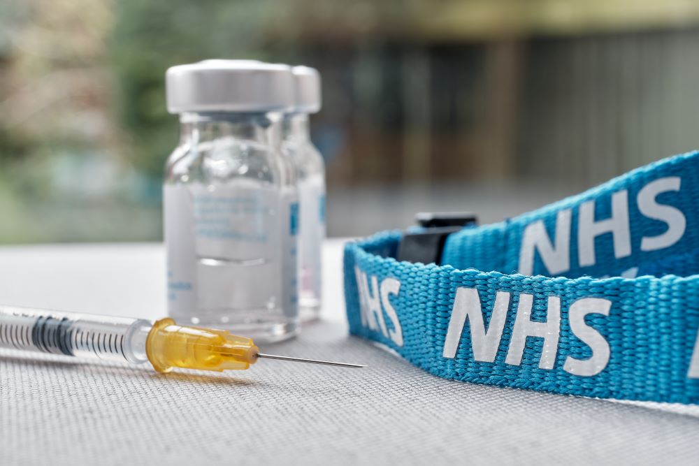 Syringe alongside vials and an NHS lanyard