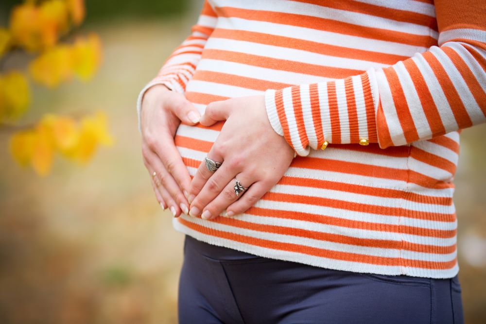 Close up of pregnant woman's bump, with autumn leaves in the background