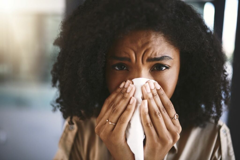 Woman blowing her nose into a tissue, looks into the camera