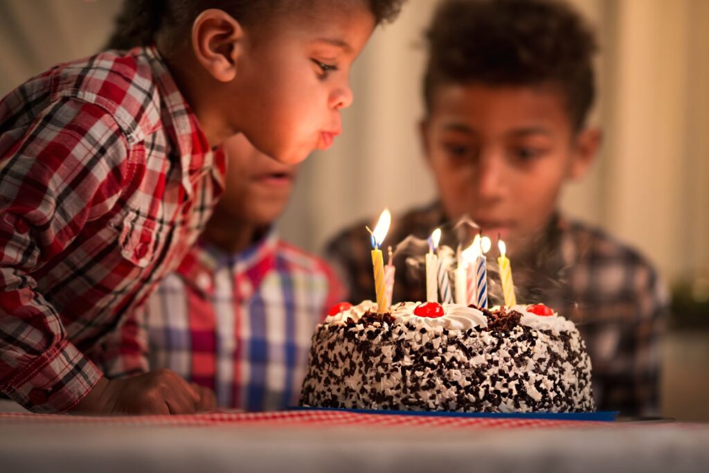 Young boy blowing out candles on a birthday cake with other children in the background