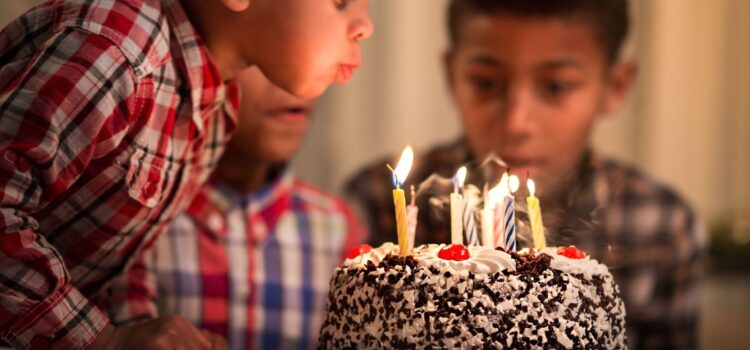 Young boy blowing out candles on a birthday cake with other children in the background