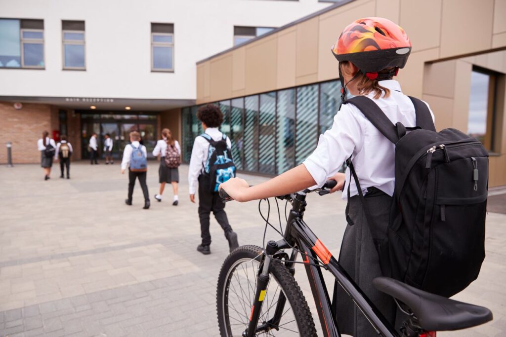 Girl wheels her bicycle towards a school entrance