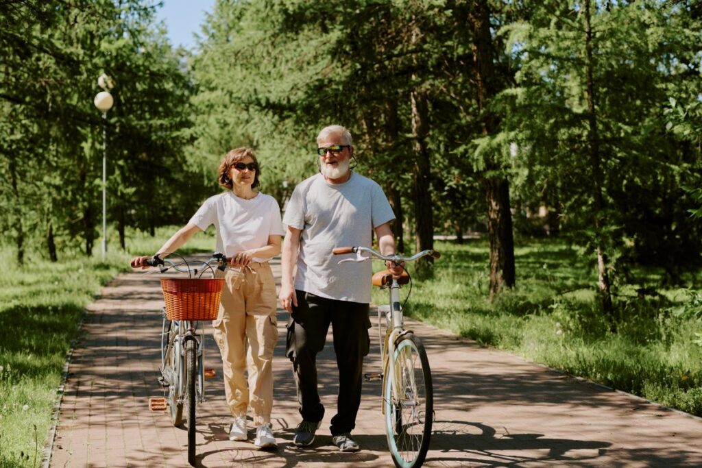 Older couple walking through a green space, wheeling their bicycles