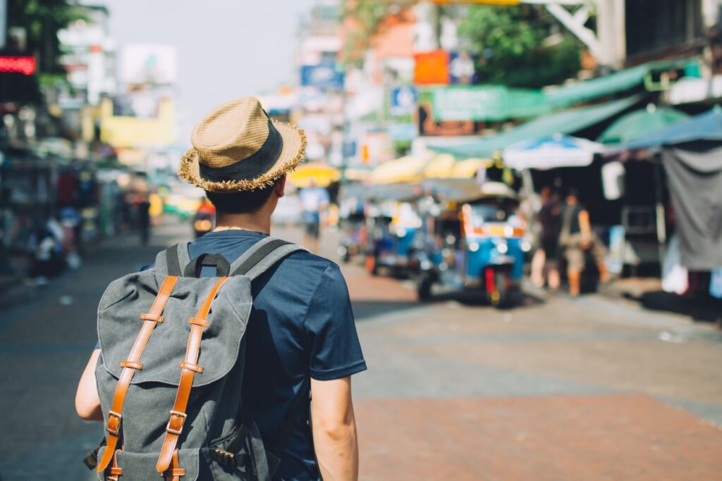 Young man wearing a hat and carrying a backpack seen from behind, in front of a street market