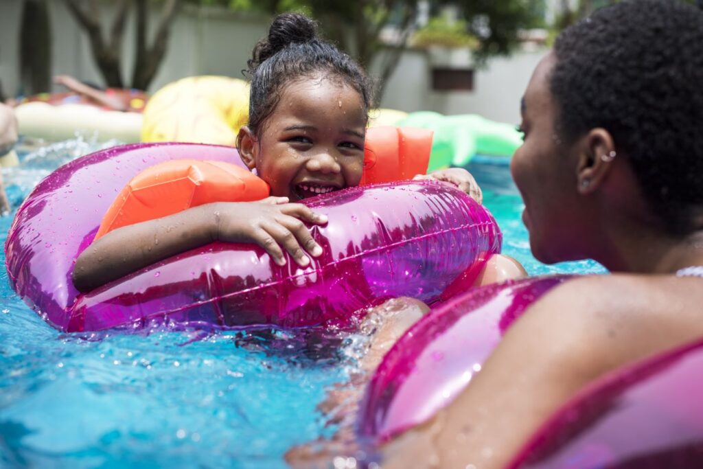 Young girl playing in a swimming pool with her mother, floating in an inflatable pink ring