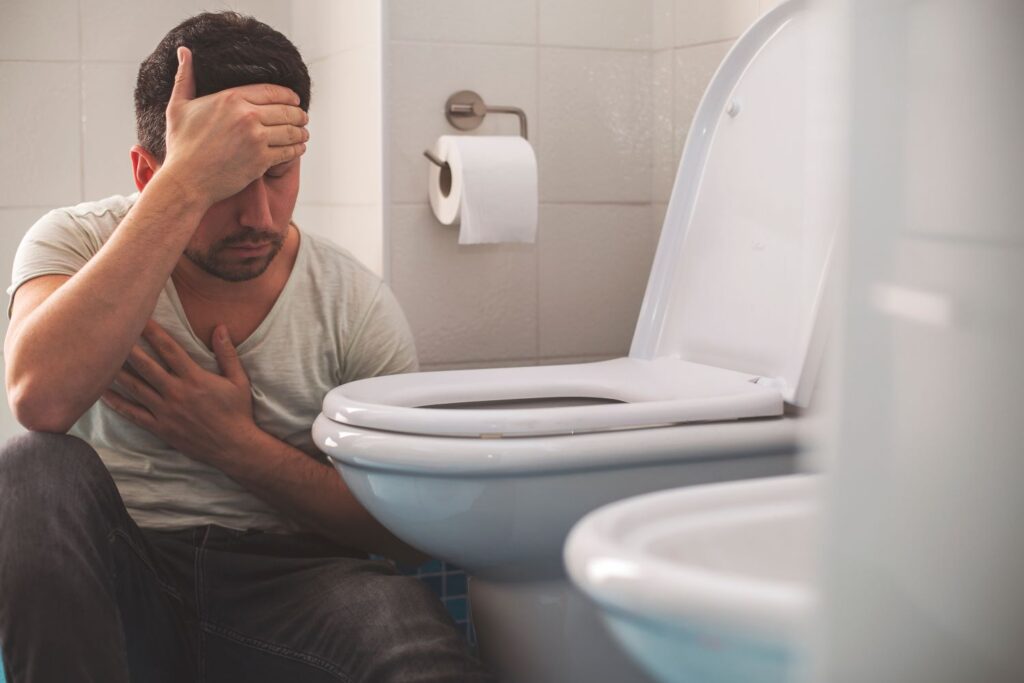 Man sits on the floor beside the toilet, clearly feeling unwell