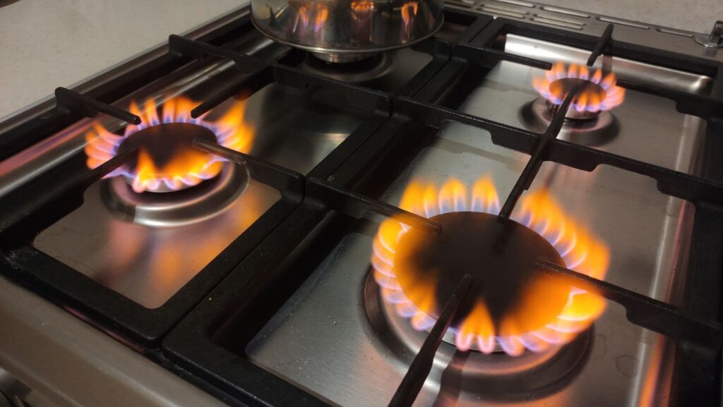 Gas hob in a kitchen with all 4 hobs burning with an orange flame