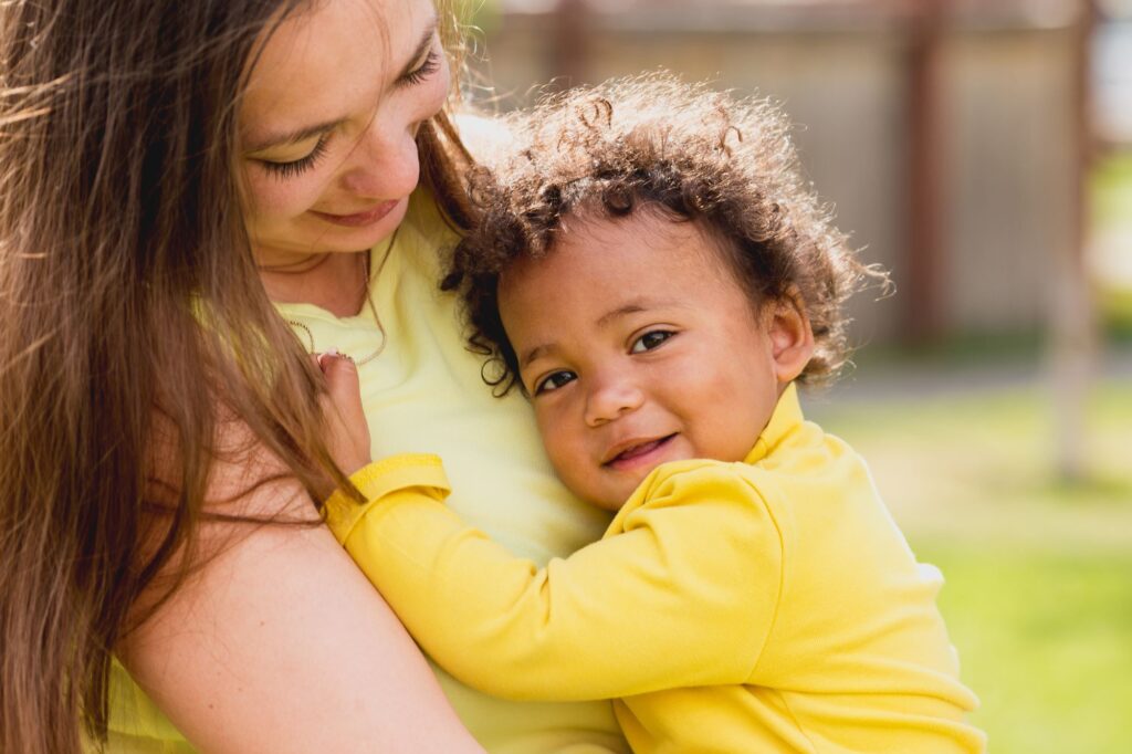 Small boy in a yellow top being held in his mother's arms