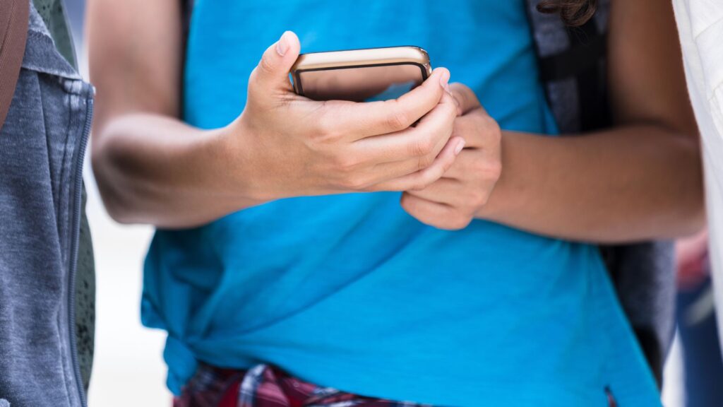 Teenager in blue top looks at their mobile phone
