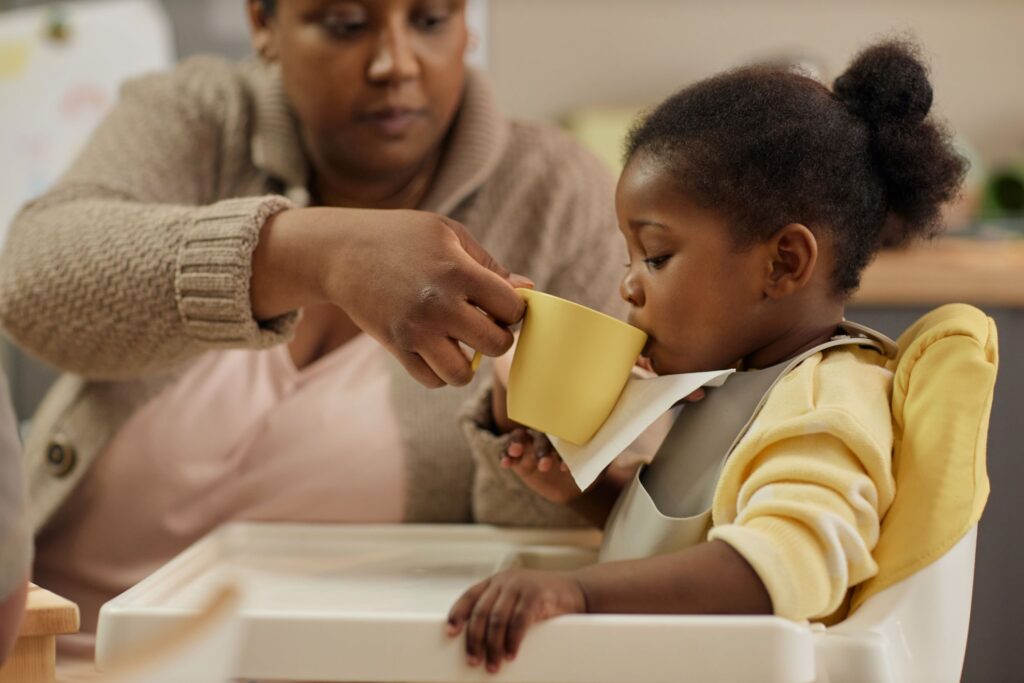 Woman helping a small child to drink out of a cup of water
