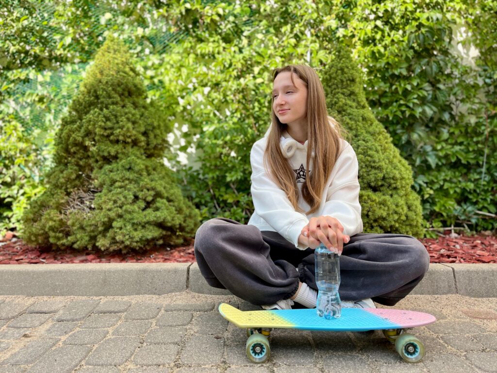 Girl sits on kerb with a bottle of water and a skateboard in front of her