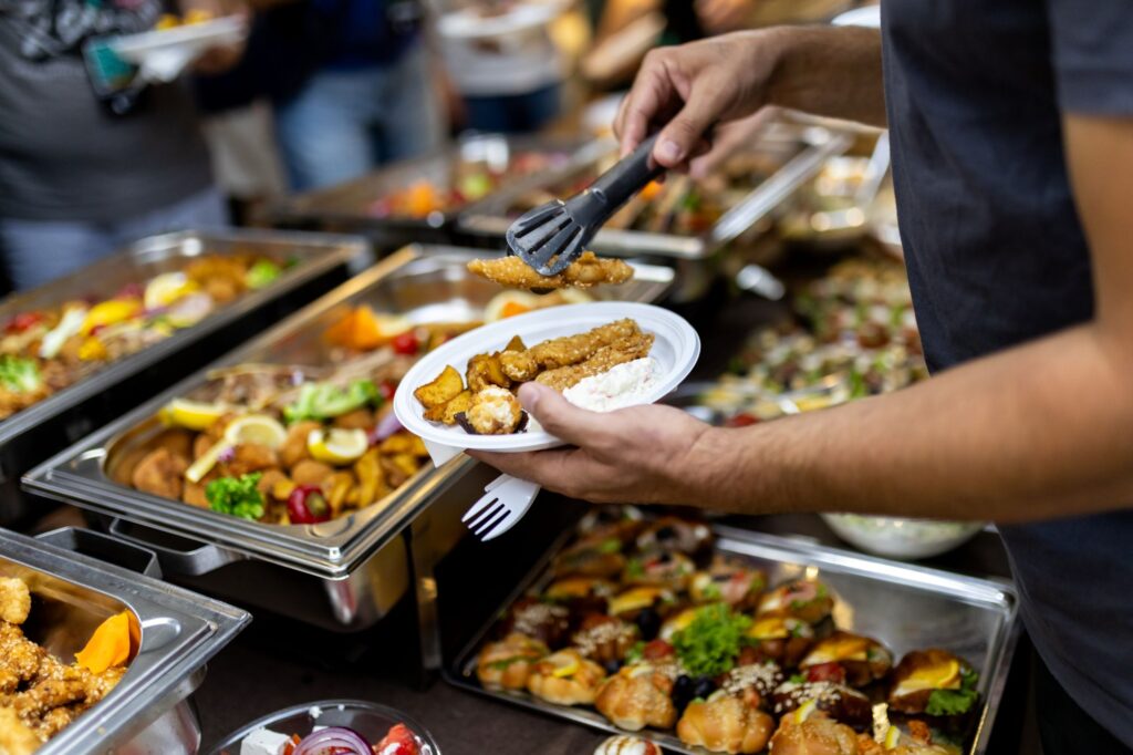 Person places food on their plate using tongs at a buffet