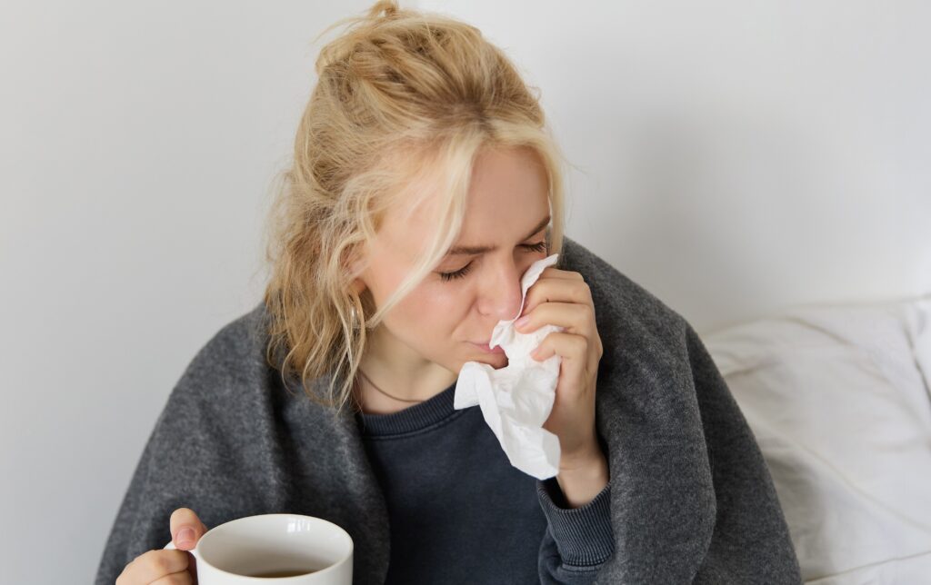 Young woman having a hot drink and blowing her nose